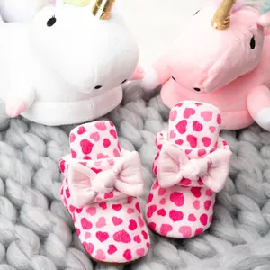 Chaussures bébé roses à semelle souple avec motifs de cœurs et nœuds sur fond tricoté