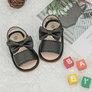 Close-up of black leather baby sandals with bow detail on a decorative nursery background