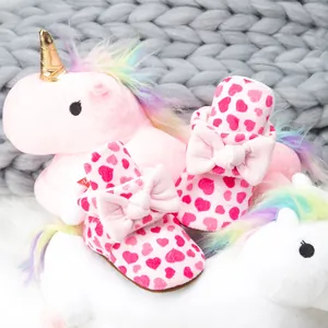 Chaussures bébé en peluche rose avec motifs cœurs et nœud sur tapis moelleux