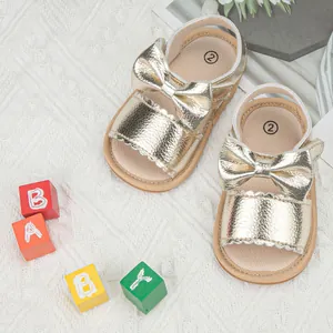 Close-up of golden faux leather baby sandals featuring large bows and scalloped edges
