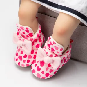 Gros plan de bottines bébé en peluche rose avec motifs cœurs et nœud décoratif