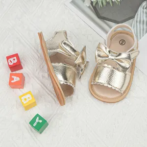 Detail of golden baby sandals with bow decoration and wavy edges on knit background