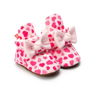 Détail de chaussons bébé roses avec motif cœur, tissu peluche doux et décor nœud
