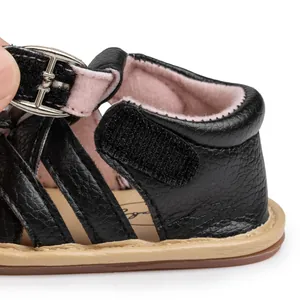 Detailed macro view of black pebbled leather and secure hook-and-loop closure for baby sandals