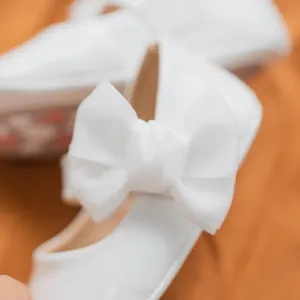 Dettaglio delle scarpe Mary Jane bianche da neonata con un grande fiocco in tessuto velato