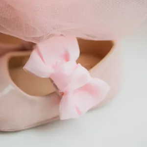 Dettaglio scarpa neonata in pelle verniciata rosa con grande fiocco di raso e pizzo