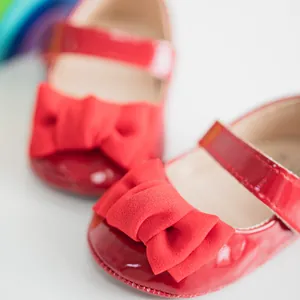 Detail von roten Lackleder-Babyschuhen mit großer Stoffschleife und Klettverschluss