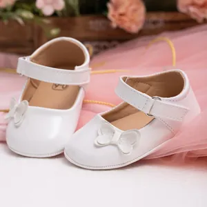 Close-up of white PU leather baby shoes with glitter bow and velcro strap detail