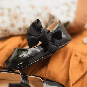 Dettaglio di scarpe da neonata in vernice nera con fiocco e suola morbida per primi passi