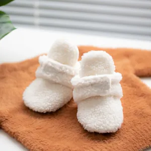 Close-up of white plush baby boots with soft soles and velcro strap closure detail