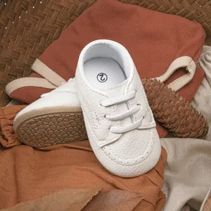 Detailed view of white baby moccasins with elastic laces and anti-slip rubber soles
