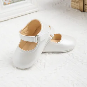 Close-up of pearl white baby Mary Jane shoes with scalloped edges and velcro straps