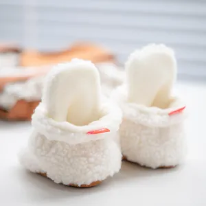 Detailed close-up of soft white fleece baby shoes with cute 3D bunny ears and red tab
