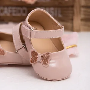 Close-up of pink faux leather baby shoes featuring a glittery bow and velcro strap