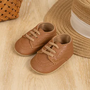 Close-up of brown leather baby brogue shoes with decorative laces on wooden background