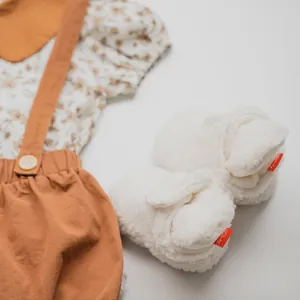 Detailed flat lay of floral baby top, corduroy overalls, and plush fleece booties