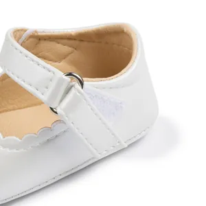 Detailed macro view of white Mary Jane baby shoes with scalloped edges and velcro strap