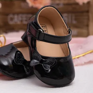 Macro detail of black patent leather baby shoes with glitter bow and velcro strap