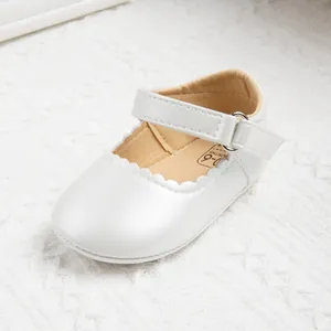 Macro detail of pearl white baby shoes with scalloped edges and 0-6 months mark