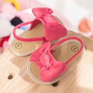 Detail of pink baby sandal with large bow, soft suede fabric and elastic heel strap