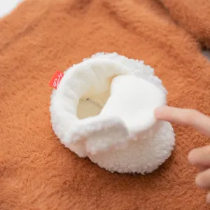 Close-up of soft white plush baby bootie featuring a red Baby label and fuzzy texture