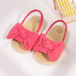 Rose pink infant summer sandals with large bow and elastic strap on white fabric