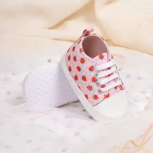 Detail view of pink baby canvas shoes with strawberry prints and non-slip dotted soles