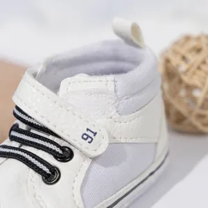 Detail of baby high-top sneakers showing white PU leather, striped laces, and velcro strap