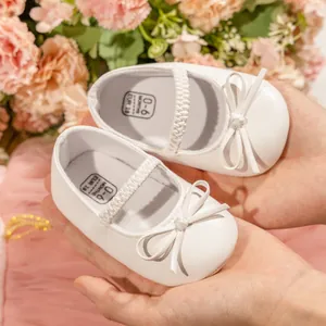 Chaussures Mary Jane blanches pour bébés avec nœud et sangle élastique en présentation à la main