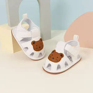 Detail view of white baby sandals with cute brown bear patch and breathable cutouts