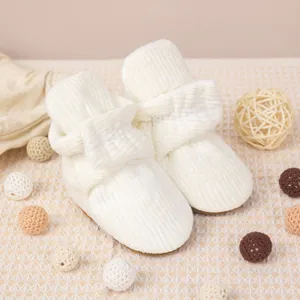 Détail du chausson bébé en maille côtelée blanche avec nœud sur un fond à carreaux beige