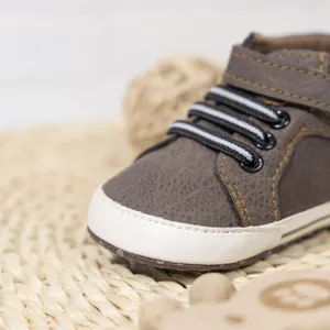 Macro shot of brown pebble-textured baby shoes with white rubber toes and striped laces