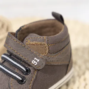 Detail of high-top baby shoes featuring brown canvas, yellow stitching, and velcro closure