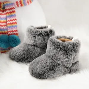 Winter plush baby boots in grey faux fur with warm brown lining on soft white carpet