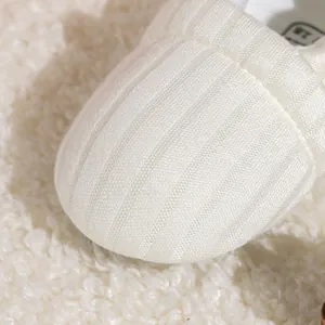 Close-up of white knitted baby shoes showing ribbed fabric texture and soft inner sole