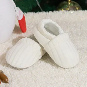 Detail of white knitted baby shoe on plush carpet with cozy Christmas decor accents