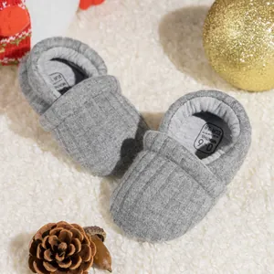 Close-up of grey knit baby walking shoe with size 18 label on a warm festive carpet