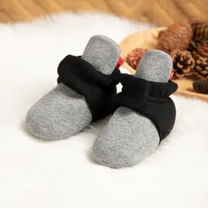 Detail von grauen Strick-Babyschuhen mit schwarzem Knöchelriemen auf weißem Kunstfellhintergrund