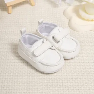 Detailed close-up of white faux leather baby shoes with velcro strap on woven mat