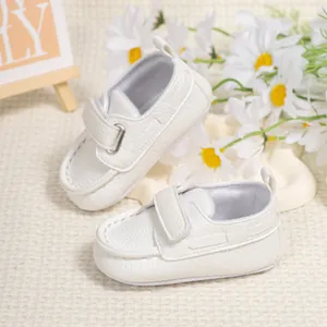 Close-up of white faux leather baby shoes with velcro strap and metal D-ring detail