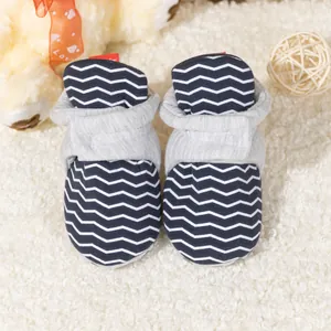 Detail von Baby-Lauflernschuhen mit grauem Wellenmuster auf flauschigem weißem Teppich
