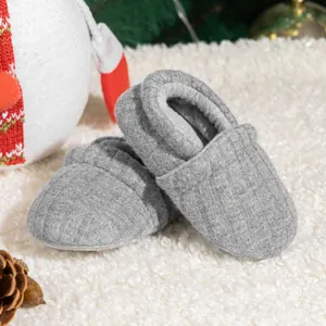 Grey knitted baby slip-on shoes with soft ribbed texture and non-slip soles on white fur