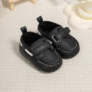 Macro shot of black pebbled leather baby loafers with velcro strap and white stitching