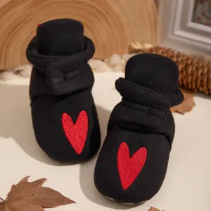 Detailansicht der gestreiften Babyschuhe mit rotem Herz-Stick auf einer Holzscheibe