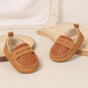 Detail of brown baby loafers featuring hand-stitched seams and woven texture on wooden background