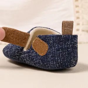 Detail of baby walking shoes showing navy woven fabric and brown velcro strap closure