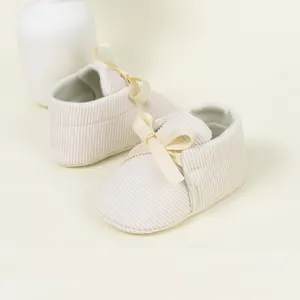 Detail of baby soft-sole shoes in beige corduroy with elegant satin bow decoration
