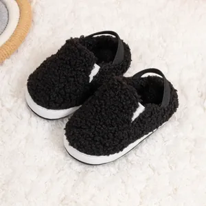 Close-up of black fuzzy baby shoes with elastic heel strap on white plush carpet