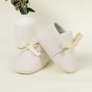 Detail of beige striped corduroy baby shoes featuring a soft sole and ribbed bow accent