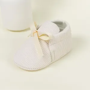 Detail of baby walking shoes in cream corduroy with a satin bow and soft non-slip sole